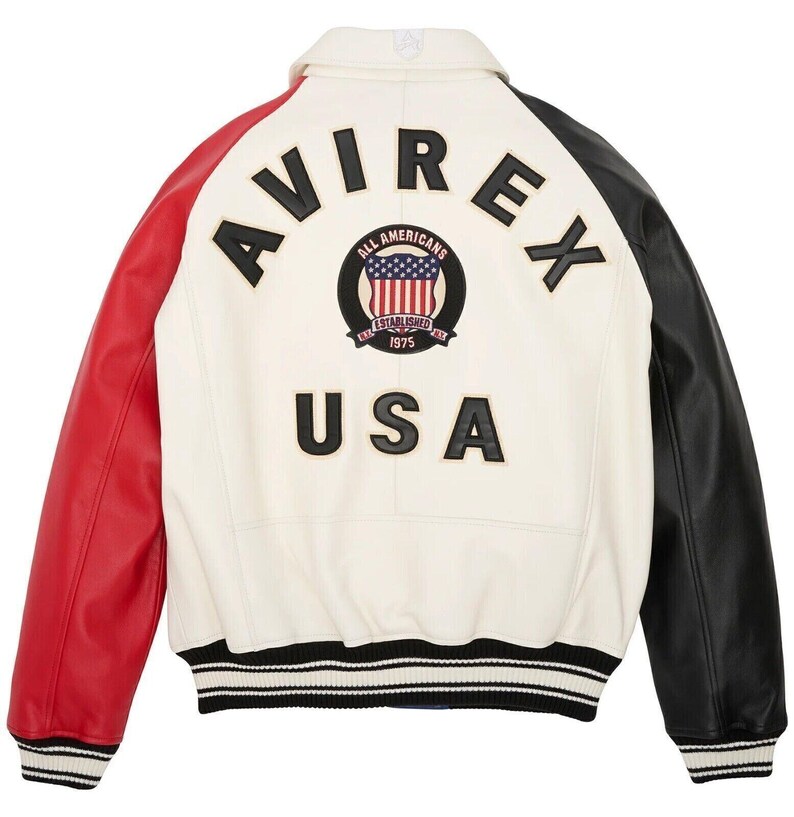May include: A cream-colored leather jacket with red and black sleeves. The back of the jacket features the word "AVIREX" above a circular patch with the American flag and the words "ALL AMERICANS ESTABLISHED 1975". Below the patch is the word "USA".