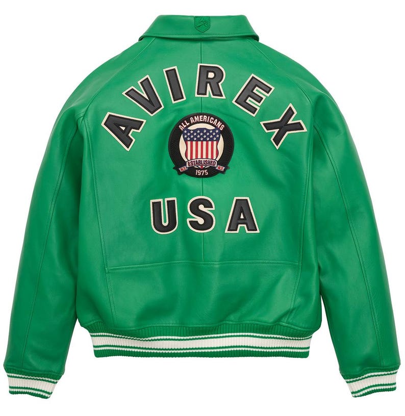 May include: A vibrant green leather jacket with the word "AVIREX" arched across the upper back. Below the text is a circular patch with the American flag and the words "ALL AMERICANS ESTABLISHED 1975". The word "USA" is below the patch. The jacket has a white and green striped hem.