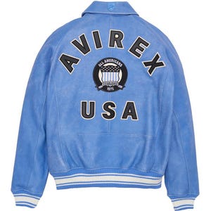 May include: Light blue leather jacket with the word "AVIREX" arched across the back, above a circular patch that reads "ALL AMERICANS ESTABLISHED 1975". Below is the word "USA". The jacket has white and blue striped cuffs and a collar.