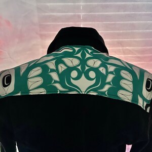 May include: Black long-sleeved shirt with a green and white patterned design on the back. The pattern features stylised leaves and geometric shapes.