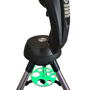 May include: A black Celestron telescope mount with a keypad and display, mounted on a silver tripod. A green, circular accessory tray with multiple holes is positioned near the base of the tripod.