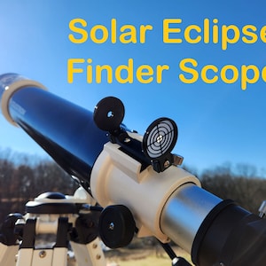 May include: A black and white telescope with a white finder scope and a black and white reticle. The telescope is mounted on a tripod and is pointed towards the sky. The text "Solar Eclipse Finder Scope" is written in yellow letters on a blue background.