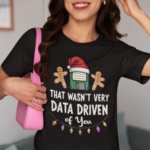 May include: Black t-shirt with the phrase "THAT WASN'T VERY DATA DRIVEN of You". The graphic includes a floppy disk wearing a Santa hat, gingerbread men, and Christmas lights.