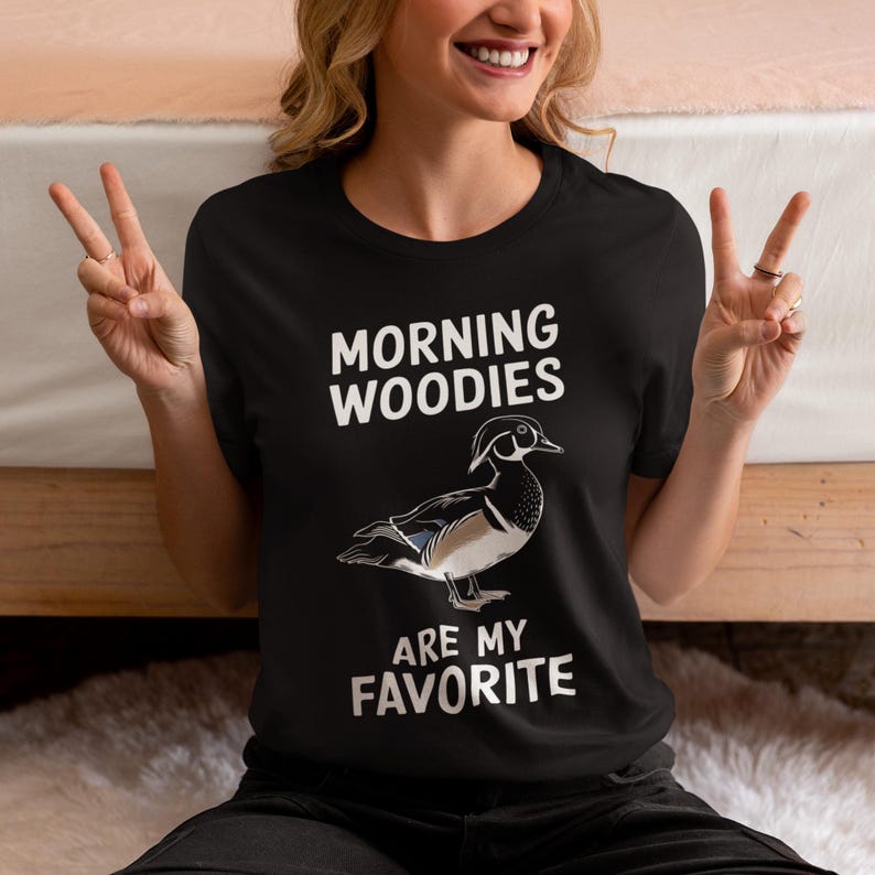 May include: A black t-shirt with white text that reads "Morning Woodies are my favorite". A cartoon image of a wood duck is printed on the shirt.