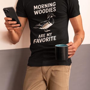 May include: A black t-shirt with a white graphic of a wood duck and the text "Morning Woodies Are My Favorite".