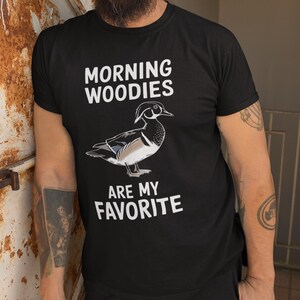 May include: A black t-shirt with white text that reads "Morning Woodies are my favorite". A cartoon wood duck is pictured above the text.