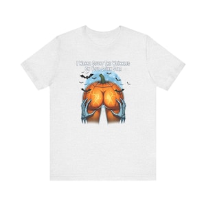 Può includere: Una t-shirt a maniche corte grigio chiaro con la grafica di una zucca arancione a forma di glutei, tenuta da due mani scheletriche. Sopra la zucca, il testo recita I WANNA COUNT THE WRINKLES ON YOUR STINK STAR, circondato da piccoli pipistrelli neri.