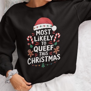 May include: Black sweatshirt with a Christmas-themed graphic. The design includes a Santa hat, candy canes, gingerbread men, and the text "MOST LIKELY TO QUEEF THIS CHRISTMAS" in white. A festive holiday apparel item.