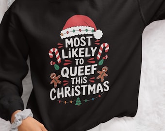 May include: Black sweatshirt featuring a Christmas graphic. The design includes a Santa hat, candy canes, gingerbread men, and the text "MOST LIKELY TO QUEEF THIS CHRISTMAS" in white. A festive holiday apparel item.