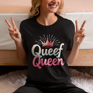 May include: Black t-shirt with a pink and blue graphic that says "Queef Queen" and features a crown with colorful jewels.