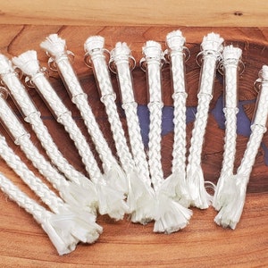 May include: A group of 18 white braided wicks with glass tubes. The wicks are arranged in a fan shape on a wooden surface.