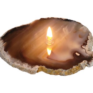 May include: A natural agate slice with a warm brown and cream color palette. A small, clear candle holder with a lit flame sits in the center, casting a soft glow and reflection. The agate has a textured, organic edge.