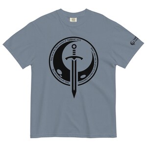 May include: A light blue t-shirt with a black circle graphic featuring a sword and a crescent moon. The text "Tune in to the final season of MONCAST" and "Don't miss out, be part of a timeless experience. Only on LifeStream VR" is written around the circle.