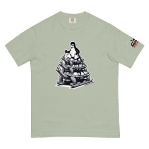 Może przedstawiać: Jasnozielony t-shirt z czarno-białą ilustracją pingwina jadącego na saniach na czterech żółwiach. Pod ilustracją znajduje się napis "sudorvi.com".