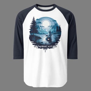May include: A white and navy blue baseball t-shirt featuring a graphic of a knight fishing in a lake under a full moon. The graphic is surrounded by a circle with the text "MOONCAST" in a stylised font.