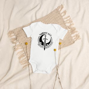 May include: White baby onesie with a black graphic of a crescent moon with a sword and the text "Mooncast Min Stats Max Cuteness".