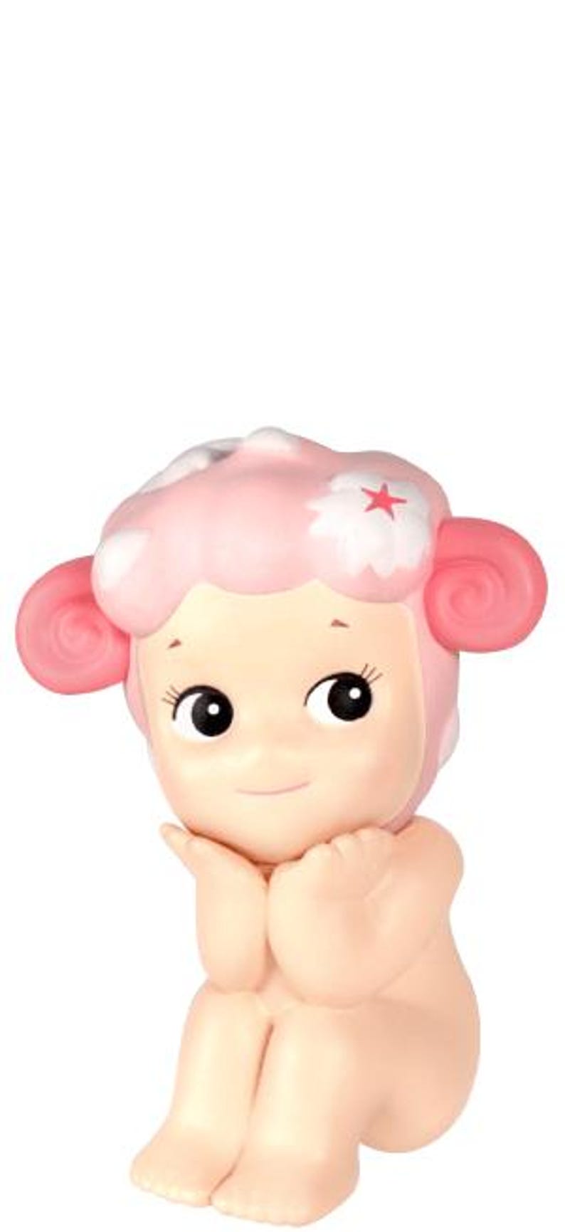 Pu&ograve; includere: Statuetta rosa chiaro di un personaggio seduto con la testa a forma di pecora. La testa ha un design rosa a forma di nuvola con una stella rossa. Il personaggio ha grandi occhi neri e si tiene le mani vicino al viso.