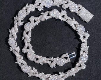 Könnte beinhalten: Eine funkelnde silberne Halskette mit einem Blumen- und Blättermuster. Die Halskette verfügt über mehrere blütenförmige Cluster und Blattakzente mit einem sicheren Verschluss. Der Schmuck ist vor einem dunklen Hintergrund platziert.