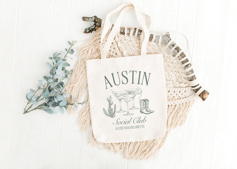 May include: A white canvas tote bag with the text "Austin Social Club Kate's Bachelorette" printed on it. The bag features a green illustration of cacti, margarita glasses, and cowboy boots.