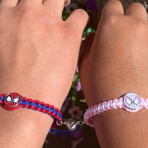 May include: Two friendship bracelets featuring a Spiderman design. One bracelet is red and blue with a silver heart charm. The other bracelet is pink and white.