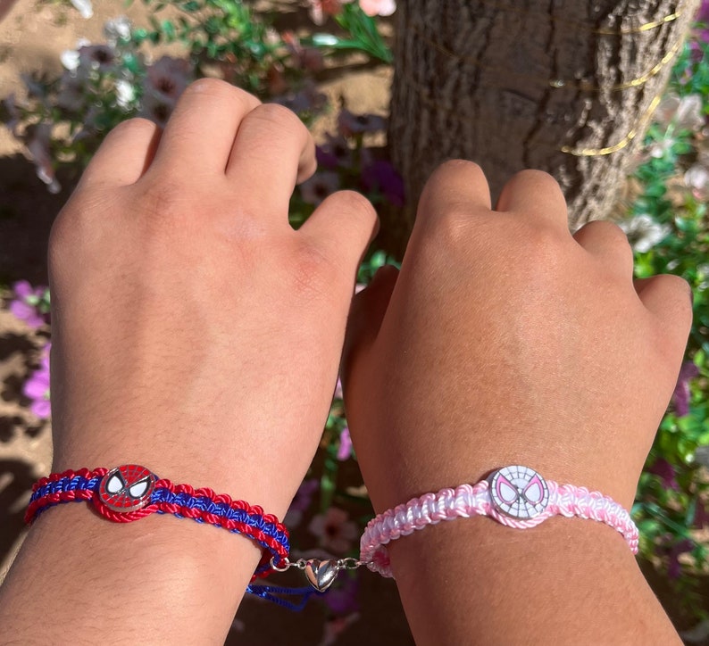 May include: Two friendship bracelets featuring a Spiderman design. One bracelet is red and blue with a silver heart charm. The other bracelet is pink and white.