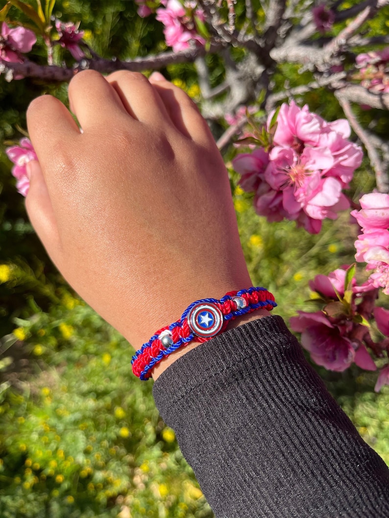 Puede incluir: Pulsera trenzada roja, blanca y azul con un dije plateado con el escudo del Capit&aacute;n Am&eacute;rica.