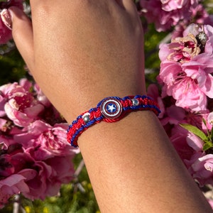 Puede incluir: Pulsera trenzada roja, blanca y azul con un dije de escudo de Capit&aacute;n Am&eacute;rica plateado.