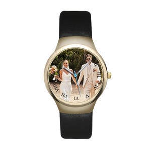 May include: A wristwatch with a gold-toned circular case and a black leather strap. The watch face features a custom photograph of a couple in wedding attire, with black Roman numerals marking the hours and silver-toned hour and minute hands.