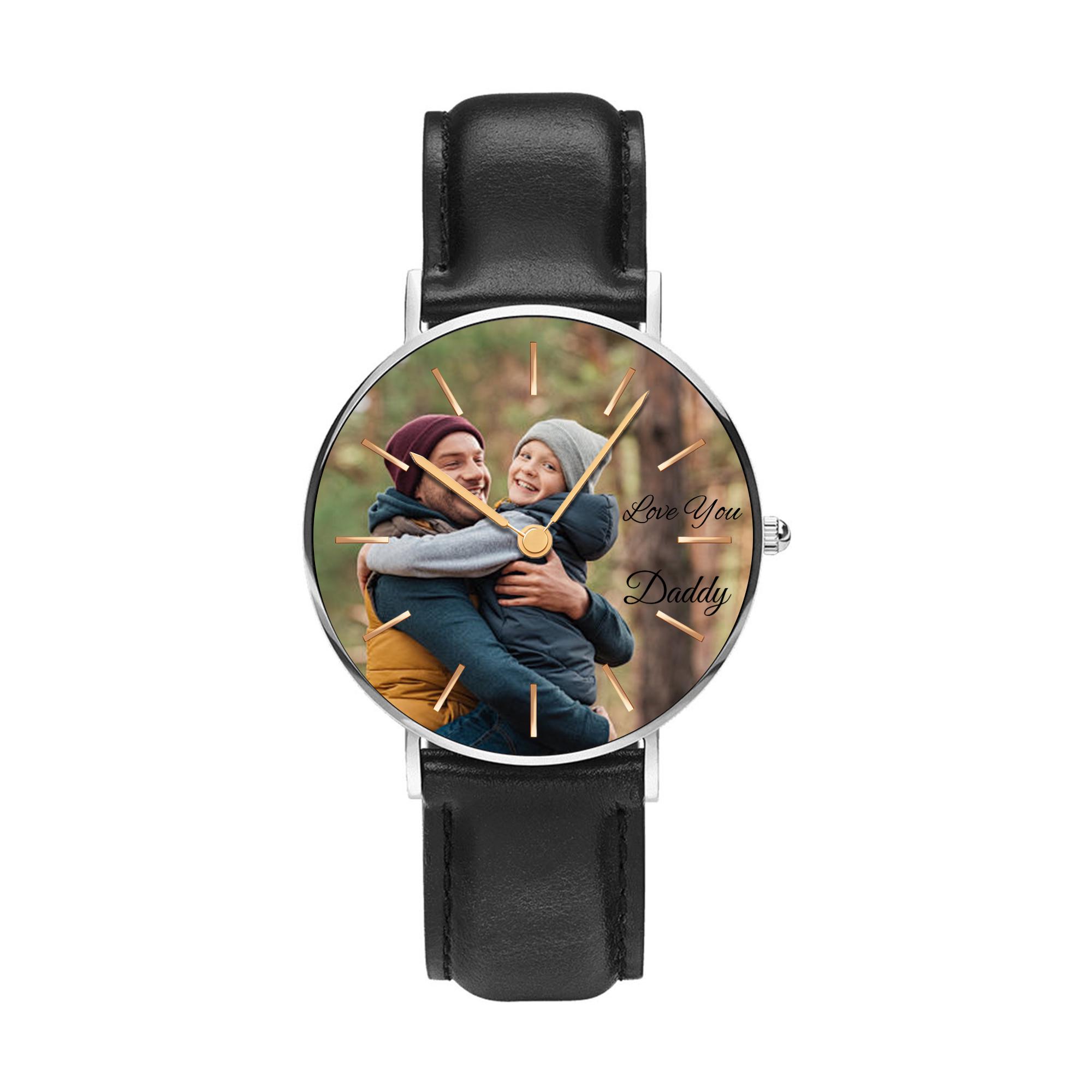 May include: A wristwatch with a black leather strap and a silver-toned circular case. The watch face features a photograph of an adult and a child embracing, with the text Love You Daddy printed in black script and thin gold-toned hour markers.
