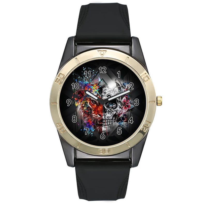 May include: A wristwatch with a black silicone strap and a dark case featuring a gold-toned bezel. The watch face displays a split graphic design with a colorful lion on the left and a monochrome skull on the right, surrounded by white numerals.