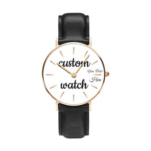 May include: A wristwatch with a black leather strap and a rose gold-toned circular case. The white watch face features thin gold-toned hour markers, gold-toned hands, and the black text "custom watch" with "You Text Here" printed on the right.