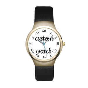 May include: A wristwatch with a gold-tone case and a black leather strap. The white dial features black Roman numerals and the text "custom watch" in a cursive script. The watch has silver-tone hour, minute, and second hands centred on the face.