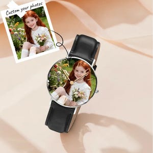 Puede incluir: Un reloj de pulsera con correa de cuero negro y caja circular plateada. La esfera del reloj presenta una fotograf&iacute;a a color personalizada de una persona joven de cabello rojo con una blusa blanca sosteniendo un ramo de flores en un jard&iacute;n.