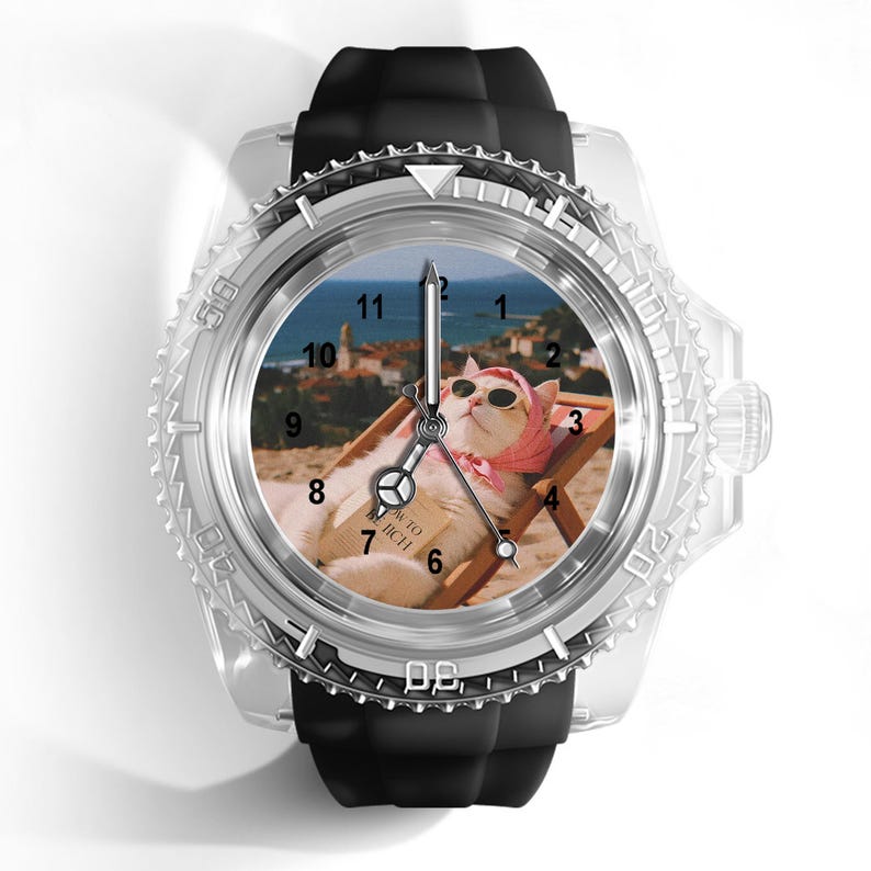 May include: A wristwatch with a black silicone strap and a clear plastic casing. The watch face features a graphic of a cat wearing sunglasses and a pink headscarf, lounging on a beach chair with a book titled How to be Rich, set against a coastal background.