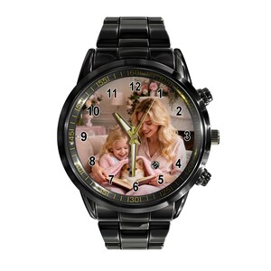 May include: A black metal wristwatch featuring a custom dial with a photograph of a person and a child reading a book with a small dog. The watch has a black link band, a round case, gold-toned hands, and black numerals from one to twelve.
