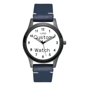 Pu&ograve; includere: Un orologio da polso con cinturino in pelle blu scuro, cassa in metallo nero e quadrante bianco. Il quadrante presenta numeri arabi neri da 1 a 12, lancette nere per ore e minuti, una sottile lancetta dei secondi rossa e il testo "LOGO Custom Watch".