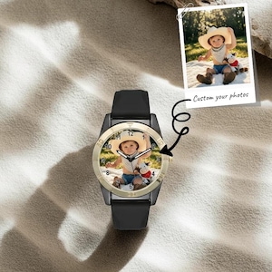 May include: A black wristwatch featuring a custom photo on the dial of a child wearing a straw hat and holding a stuffed cow toy. The watch has a black silicone strap, a gold-toned bezel, and black hour, minute, and second hands.