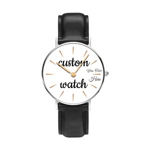 May include: A wristwatch with a black leather strap and a silver-tone circular case. The white dial features gold-tone hour markers, gold-tone hands, and the black text "custom watch" with "You Text Here" printed on the right side of the face.