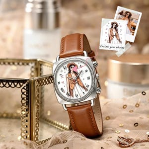 May include: A square-faced wristwatch with a brown leather strap and a silver-toned bezel. The white watch face features a central illustration of a person wearing a hat and vest, surrounded by Roman numerals, stars, and hearts. Two small photos are attached.