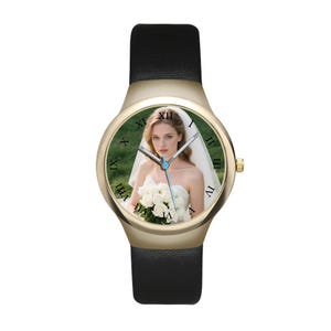 May include: A wristwatch with a gold-tone round case and a black leather strap. The watch face features a photographic print of a person in a white wedding dress holding a bouquet of white roses, with black Roman numerals marking the hours.