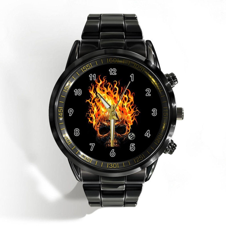 May include: A black stainless steel wristwatch featuring a round face with a graphic of a skull engulfed in orange and yellow flames. The dial displays white Arabic numerals from 1 to 12, gold-toned hands, and a small date window at the 4 o'clock position.