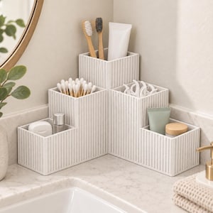 May include: A white, tiered corner bathroom organizer with a vertical ribbed texture. The unit features five distinct compartments of varying heights, currently holding toothbrushes, cotton swabs, dental floss, and various small toiletry containers.