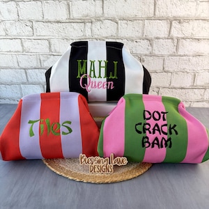 May include: Three structured pouches with vertical stripes. The top pouch is black and white with green and pink text reading "MAHJ Queen". The bottom left is red and light purple with green text "Tiles". The bottom right is green and pink with black text "DOT CRACK BAM".