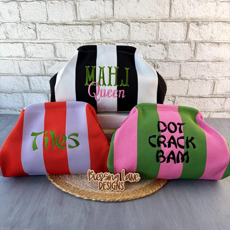 May include: Three structured pouches with vertical stripes. The top pouch is black and white with green and pink text reading "MAHJ Queen". The bottom left is red and light purple with green text "Tiles". The bottom right is green and pink with black text "DOT CRACK BAM".