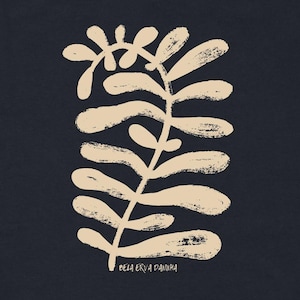 May include: A black short-sleeved t-shirt featuring a beige, textured botanical illustration of a leafy plant stem. Below the plant graphic, the text "BELA ERVA DANINHA" is printed in a small, simple font. The shirt has a crew neckline.