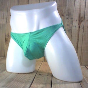 Può includere: Un paio di slip verde tinta unita con taglio a vita bassa e tasca frontale sagomata. Il capo è esposto su un busto di manichino bianco, mettendo in risalto il tessuto liscio e il design minimalista dell'intimo con sottili fasce laterali.