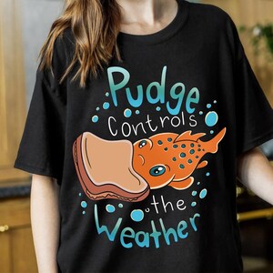a woman wearing a t - shirt that says pudge controls the weather