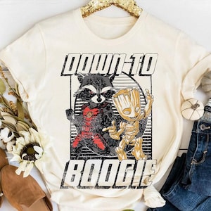 May include: Cream-colored t-shirt featuring a graphic of Rocket Raccoon and Groot from Guardians of the Galaxy. The raccoon is in a red and black outfit, and Groot is gold. The text "DOWN-TO BOOGIE" is printed above and below the characters.
