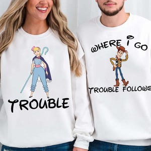 Two people wearing white sweatshirts with cartoon characters and text printed on them.