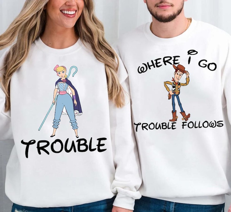 Two people wearing white sweatshirts with cartoon characters and text printed on them.
